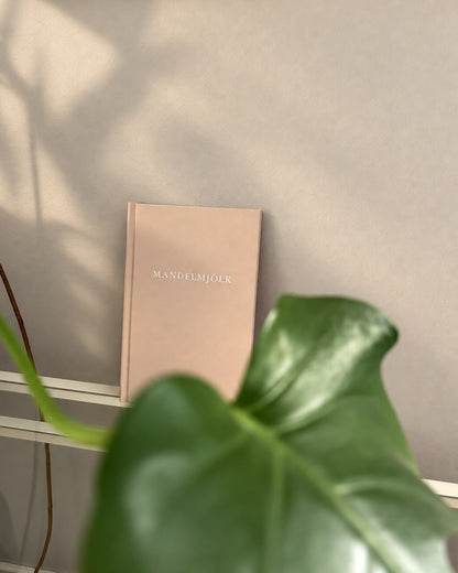 Beige Mandelmjölk anteckningsbok bakom ett monsterablad i mjukt solljus